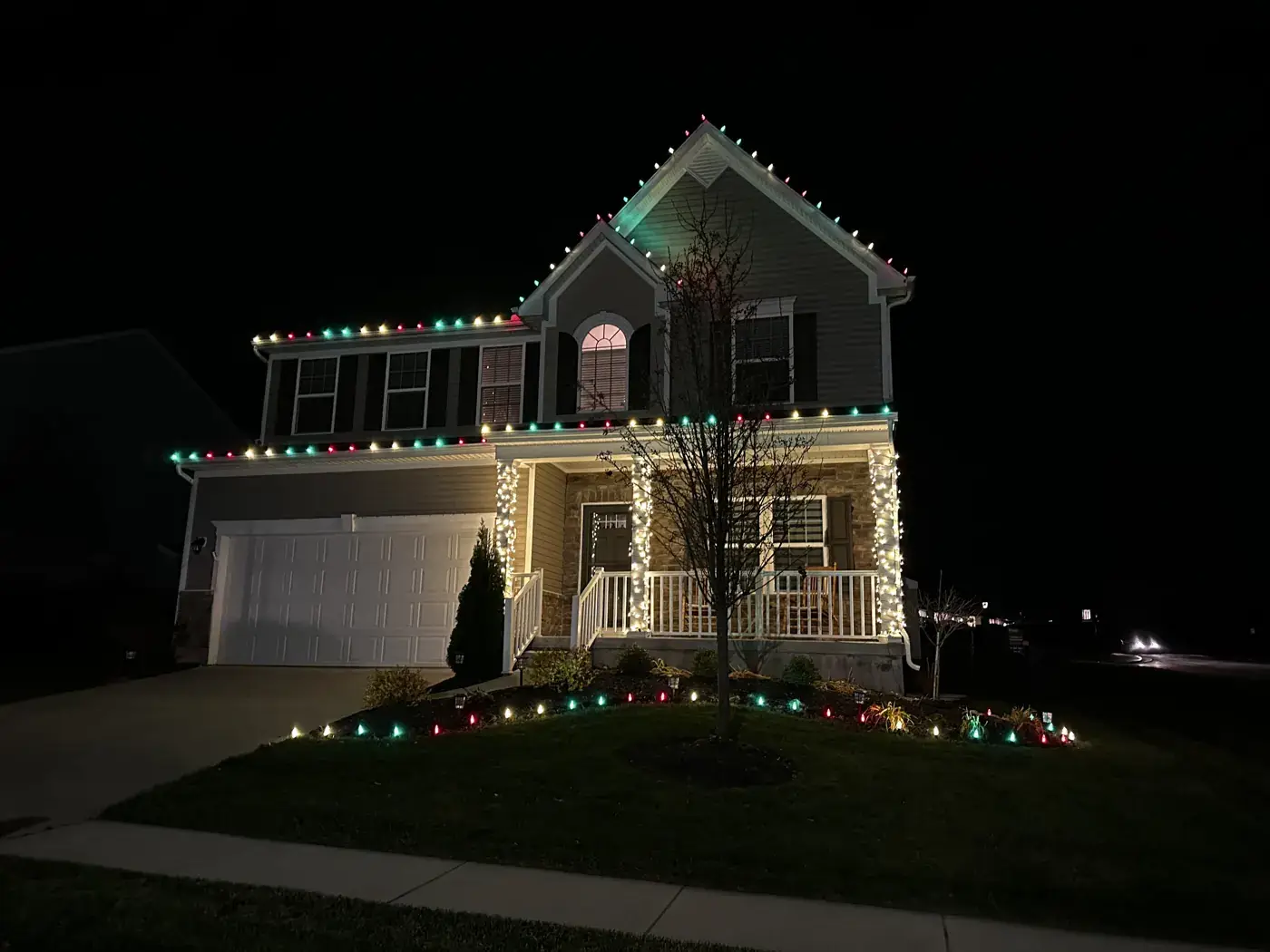 Christmas Light Installation in Miami Heights, OH Red and green Christmas roofline lights with wrapped porch posts on a two-story home