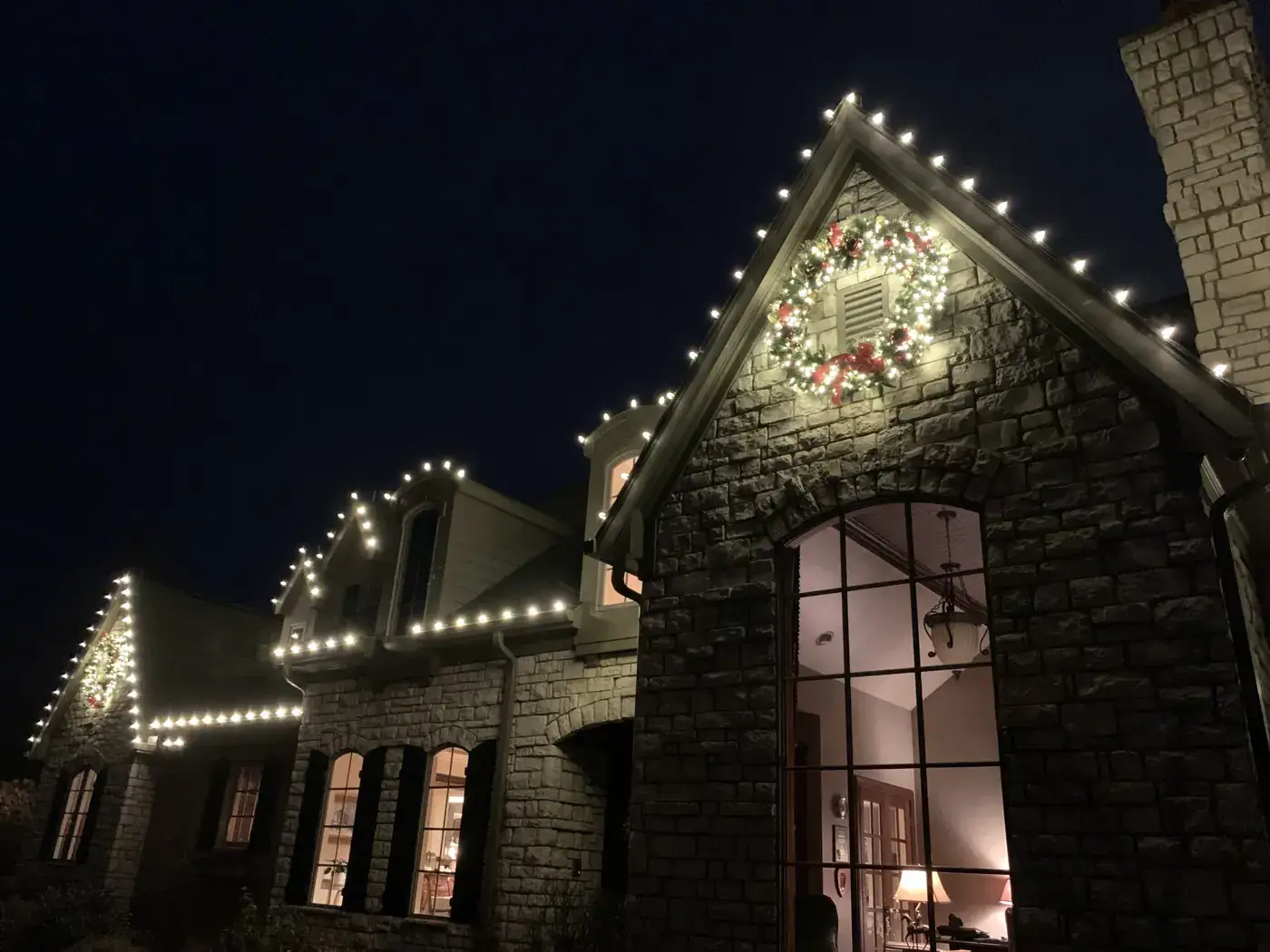 Christmas Light Installation in Villa Hills, KY Christmas lights and a wreath on a stone home gable with a tall lit window